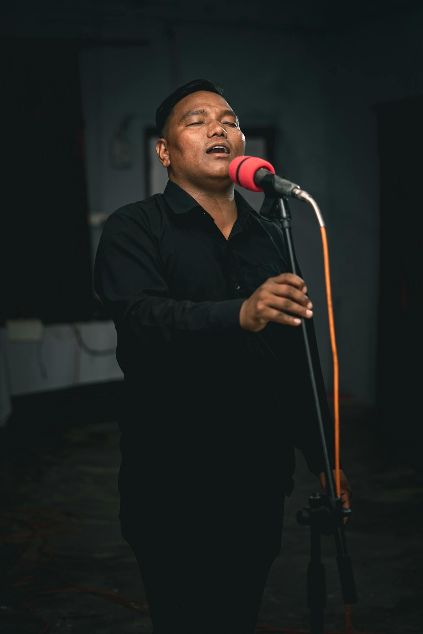 Male singer passionately performing into a microphone with eyes closed, creating an intimate atmosphere.